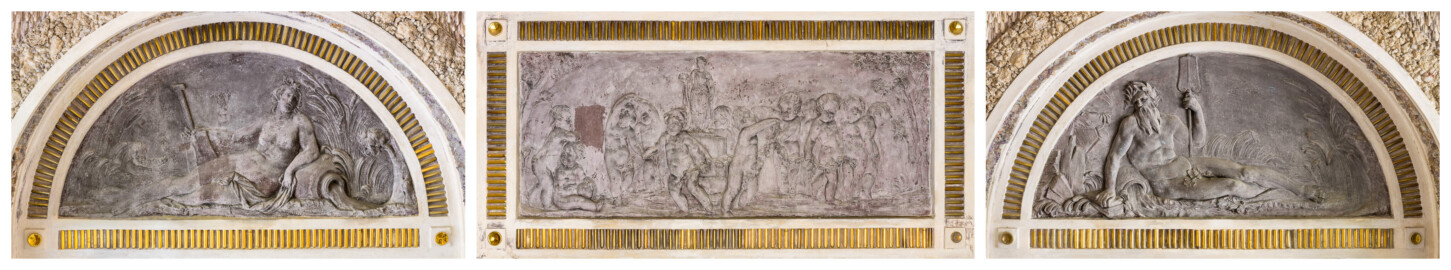 Schloss und Schlossgarten Schwetzingen - Garten - Badhausanlage - Östliches Achathäuschen - v.l.n.r.: Nordwand, Ostwand, Südwand - Blick auf zwei Lünetten und ein Rechteckfeld mit Bleireliefs; links: Darstellung einer Quellennymphe, von Schilfgras eingerahmt; linker Arm gestützt auf Urne, aus der Wasser fließt; rechter Arm ein Ruder haltend; links ein Putto im Schilf; Mitte: Darstellung eines Erotentanzes um die Statue der Göttin Flora; Flora auf einem Podest stehend, in der Rechten ein Blumenkranz; zehn Putti im Ringeltanz um Flora, teils durch eine Girlande verbunden; links zwei weitere Putti, einander liebkosend; Szene links und rechts eingerahmt durch Bäume; rechts: Darstellung eines bärtigen Flussgottes, gegen einen Felsen lehnend, umgeben von Schilfgras; rechte Hand auf Steine gestützt, mit linker Hand ein Ruder haltend; zwischen rechtem Arm und Hüft eine Urne, aus der Wasser läuft (Bildhauer: Franz Conrad Linck (1730-1793), Datierung: um 1770-1775, Material: Blei, Signatur am mittleren Relief, unten rechts (schwach lesbar): "Linck. F", Breite x Höhe: ca. 125 x 58 Zentimeter) (Achathäuschen: Abmessungen Breite x Tiefe x Höhe 3,2 x 3,0 x 6,4 Meter, Innenraum Breite x Tiefe ca. 2 x 2 Meter; Architekt: Nicolas de Pigage, Fertigstellung: um 1775, Instandsetzung: 1991 - 1995) (aufgenommen im Mai 2026, am späten Vormittag) Schloss und Schlossgarten Schwetzingen - Garten - Badhausanlage - Östliches Achathäuschen - v.l.n.r.: Nordwand, Ostwand, Südwand - Blick auf zwei Lünetten und ein Rechteckfeld mit Bleireliefs; links: Darstellung einer Quellennymphe, von Schilfgras eingerahmt; linker Arm gestützt auf Urne, aus der Wasser fließt; rechter Arm ein Ruder haltend; links ein Putto im Schilf; Mitte: Darstellung eines Erotentanzes um die Statue der Göttin Flora; Flora auf einem Podest stehend, in der Rechten ein Blumenkranz; zehn Putti im Ringeltanz um Flora, teils durch eine Girlande verbunden; links zwei weitere Putti, einander liebkosend; Szene links und rechts eingerahmt durch Bäume; rechts: Darstellung eines bärtigen Flussgottes, gegen einen Felsen lehnend, umgeben von Schilfgras; rechte Hand auf Steine gestützt, mit linker Hand ein Ruder haltend; zwischen rechtem Arm und Hüft eine Urne, aus der Wasser läuft (Bildhauer: Franz Conrad Linck (1730-1793), Datierung: um 1770-1775, Material: Blei, Signatur am mittleren Relief, unten rechts (schwach lesbar): "Linck. F", Breite x Höhe: ca. 125 x 58 Zentimeter) (Achathäuschen: Abmessungen Breite x Tiefe x Höhe 3,2 x 3,0 x 6,4 Meter, Innenraum Breite x Tiefe ca. 2 x 2 Meter; Architekt: Nicolas de Pigage, Fertigstellung: um 1775, Instandsetzung: 1991 - 1995) (aufgenommen im Mai 2026, am späten Vormittag)