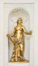 Schloss und Schlossgarten Schwetzingen - Garten - Badhaus - Von innen - Ovalsaal - Nordwestliche Wandnische - Blick auf eine blütenstreuende Frauenfigur, mit der Rechten einen Gewandbausch mit Blüten raffend, in der linken Hand einen  Blütenbüschel haltend; eine Begleiterin der Aurora, für den Tagesablauf stehend (Bildhauer: Peter Anton von Verschaffelt (1710-1793), Datierung: um 1779, Material: Sandstein, bronziert, Höhe 150 cm) (Gesamter Bau: Länge x Breite ca. 18 x 14 Meter, Höhe ca. 10 Meter; Architekt: Nicolas de Pigage (1723-1796); Bauzeit: 1768-1772; Gesamtinstandsetzung innen und außen: 1999-2006) (aufgenommen im Juli 2026, am frühen Nachmittag)