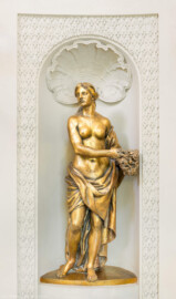 Schloss und Schlossgarten Schwetzingen - Garten - Badhaus - Von innen - Ovalsaal - Südwestliche Wandnische - Blick auf eine blütenstreuende Frauenfigur, ein Blumenbukett neben der linken Hüfte, mit der rechten Hand Blüten pflückend; eine Begleiterin der Aurora, für den Tagesablauf stehend (Bildhauer: Peter Anton von Verschaffelt (1710-1793), Datierung: um 1779, Material: Sandstein, bronziert, Höhe 150 cm) (Gesamter Bau: Länge x Breite ca. 18 x 14 Meter, Höhe ca. 10 Meter; Architekt: Nicolas de Pigage (1723-1796); Bauzeit: 1768-1772; Gesamtinstandsetzung innen und außen: 1999-2006) (aufgenommen im Juli 2026, am frühen Nachmittag)