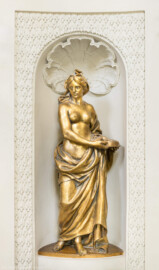 Schloss und Schlossgarten Schwetzingen - Garten - Badhaus - Von innen - Ovalsaal - Nordöstliche Wandnische - Blick auf eine Frauenfigur, ein Sieb mit beiden Händen neben ihrer linken Hüfte haltend; eine Begleiterin der Aurora, für den Tagesablauf stehend (Bildhauer: Peter Anton von Verschaffelt (1710-1793), Datierung: um 1779, Material: Sandstein, bronziert, Höhe 150 cm) (Gesamter Bau: Länge x Breite ca. 18 x 14 Meter, Höhe ca. 10 Meter; Architekt: Nicolas de Pigage (1723-1796); Bauzeit: 1768-1772; Gesamtinstandsetzung innen und außen: 1999-2006) (aufgenommen im Juli 2026, am frühen Nachmittag)