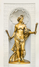 Schloss und Schlossgarten Schwetzingen - Garten - Badhaus - Von innen - Ovalsaal - Südöstliche Wandnische - Blick auf eine Frauenfigur mit brennenden Fackeln in beiden ausgestreckten Armen; eine Begleiterin der Aurora, für den Tagesablauf stehend (Bildhauer: Peter Anton von Verschaffelt (1710-1793), Datierung: um 1779, Material: Sandstein, bronziert, Höhe 150 cm) (Gesamter Bau: Länge x Breite ca. 18 x 14 Meter, Höhe ca. 10 Meter; Architekt: Nicolas de Pigage (1723-1796); Bauzeit: 1768-1772; Gesamtinstandsetzung innen und außen: 1999-2006) (aufgenommen im Juli 2026, am frühen Nachmittag)