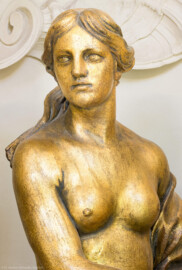 Schloss und Schlossgarten Schwetzingen - Garten - Badhaus - Von innen - Ovalsaal - Südwestliche Wandnische - Detailansicht des Oberkörpers einer blütenstreuenden Frauenfigur, ein Blumenbukett neben der linken Hüfte, mit der rechten Hand Blüten pflückend; eine Begleiterin der Aurora, für den Tagesablauf stehend (Bildhauer: Peter Anton von Verschaffelt (1710-1793), Datierung: um 1779, Material: Sandstein, bronziert, Höhe 150 cm) (Gesamter Bau: Länge x Breite ca. 18 x 14 Meter, Höhe ca. 10 Meter; Architekt: Nicolas de Pigage (1723-1796); Bauzeit: 1768-1772; Gesamtinstandsetzung innen und außen: 1999-2006) (aufgenommen im Juli 2026, am späten Nachmittag)
