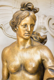 Schloss und Schlossgarten Schwetzingen - Garten - Badhaus - Von innen - Ovalsaal - Südöstliche Wandnische - Detailansicht des Oberkörpers einer Frauenfigur mit brennenden Fackeln in beiden ausgestreckten Armen; eine Begleiterin der Aurora, für den Tagesablauf stehend (Bildhauer: Peter Anton von Verschaffelt (1710-1793), Datierung: um 1779, Material: Sandstein, bronziert, Höhe 150 cm) (Gesamter Bau: Länge x Breite ca. 18 x 14 Meter, Höhe ca. 10 Meter; Architekt: Nicolas de Pigage (1723-1796); Bauzeit: 1768-1772; Gesamtinstandsetzung innen und außen: 1999-2006) (aufgenommen im Juli 2026, am späten Nachmittag)