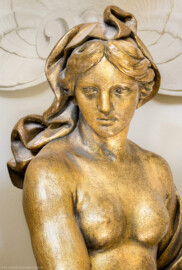 Schloss und Schlossgarten Schwetzingen - Garten - Badhaus - Von innen - Ovalsaal - Nordöstliche Wandnische - Detailansicht des Oberkörpers einer Frauenfigur, ein Sieb mit beiden Händen neben ihrer linken Hüfte haltend; eine Begleiterin der Aurora, für den Tagesablauf stehend (Bildhauer: Peter Anton von Verschaffelt (1710-1793), Datierung: um 1779, Material: Sandstein, bronziert, Höhe 150 cm) (Gesamter Bau: Länge x Breite ca. 18 x 14 Meter, Höhe ca. 10 Meter; Architekt: Nicolas de Pigage (1723-1796); Bauzeit: 1768-1772; Gesamtinstandsetzung innen und außen: 1999-2006) (aufgenommen im Juli 2026, am späten Nachmittag)