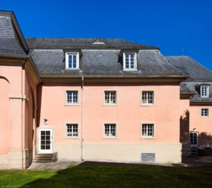 Schloss und Schlossgarten Schwetzingen - Garten - Schlosstheater - Von Osten - Blick von der Südostseite des Gesandtenhausgartens auf den südlichen Teil der Ostfassade des Schlosstheaters; ganz links die Rückseite des nördlichen Zirkelbaus; die (Notausgangs-) Tür links führt in das südöstliche Treppenhaus; die beiden Fenster links des Regenrohrs gehören zum Treppenhaus, die vier Fenster rechts davon zu den Foyers im Erdgeschoss und 1. Obergeschoss; die (Notausgangs-) Tür rechts führt in das Foyer des Erdgeschosses; die beiden Fenster ganz rechts gehören zu den Foyers im 1. und 2. Obergeschoss (Gesamter Bau: Länge x Breite: ca. 62 x 35 Meter; Architekt: Nicolas de Pigage (1723-1796); Bauzeit: 1752-1753, Erweiterung 1762, Sanierung: 1937, Renovierung: 1952, Generalsanierung / Umbau 1971-1974, Restaurierung: 1999-2005) (aufgenommen im Juli 2026, am späten Vormittag)