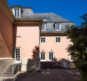 Schloss und Schlossgarten Schwetzingen - Garten - Schlosstheater - Von Osten - Blick vom Gesandtenhausgarten auf den nördlichen Teil der Ostfassade des Schlosstheaters; die drei (Notausgangs-) Türen links und in der Mitte führen in das Foyer des Erdgeschosses, die (Notausgangs-) Tür ganz rechts führt in das nordöstliche Treppenhaus (Gesamter Bau: Länge x Breite: ca. 62 x 35 Meter; Architekt: Nicolas de Pigage (1723-1796); Bauzeit: 1752-1753, Erweiterung 1762, Sanierung: 1937, Renovierung: 1952, Generalsanierung / Umbau 1971-1974, Restaurierung: 1999-2005) (aufgenommen im Juli 2026, am späten Vormittag)