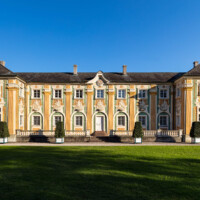 Schloss Bruchsal - Nördliche Orangerie / Nebendienstdienerbau - Von Außen / Von Westen - Blick von der Schlossterrasse auf die Westfassade der Orangerie (ursprünglich gemalt von Giovanni Francesco Marchini, zwischen 1732 und 1737, restauriert von Josef Mariano Kitschker, zwischen 1900 und 1910, erneut restauriert von Klaus Siller (Fassadenmalerei) und Walter Maschke (Allegorien), 1976) (aufgenommen im Oktober 2018, am späten Nachmittag)
