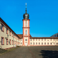 Schloss Bruchsal - Kirchturm / Finsterer Gang / Verbindungsgang - Von Außen / Von Osten - Blick vom ehemaligen südlichen Marstall (heute Parkplatz) auf den Kirchturm der Hofkirche und den Finsteren Gang, links der Seminarbau / die Pagerie, rechts der Kirchenflügel / die Hofkirche (aufgenommen im August 2019, am Vormittag)