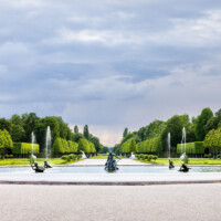 Schloss und Schlossgarten Schwetzingen - Garten - Hauptachse Ost-West / Kreisparterre - Von Osten - Blick nach Westen auf den Arionbrunnen, entlang der Ost-West-Achse, im Hintergrund die Pfalz mit dem 670 Meter hohen Kalamit (aufgenommen im Mai 2023, am frühen Abend)