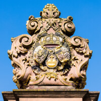 Schloss und Schlossgarten Schwetzingen - Schloss - Ehrenhof / Cour d'honneur - Eingangstor, linker / südlicher Torpfosten - Von Osten - Blick nach oben auf das Wappen von Kurfürst Johann Wilhelm (1658-1716, reg. 1690-1716); Bildhauer: Joseph Mauchert, Datierung: um 1713; ursprünglicher Aufstellungsort des Torpfostens mit dem Wappen: hinter der Brücke, um 1748 bei der Anlage des Marktplatzes vor der Brücke aufgestellt (aufgenommen im Juni 2023, am Vormittag)