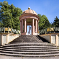 Schloss und Schlossgarten Schwetzingen - Garten - Anlage Apollotempel - Von außen - Von Westen - Blick von der unteren Terrasse auf die Treppe zur oberen Terrasse mit dem schmiedeeisernen Geländer mit Sonnengesichtern sowie auf den Rundtempel (Monopteros) des Apollo (mit zwölf Säulen ionischer Säulenordnung, ohne Cella), darin eine Statue des Apollo beim linkshändigen Lyra-Spiel (Skulptur geschaffen von Peter Anton von Verschaffelt, vor 1773) (Anlage: Länge x Breite: ca. 30 x 20 Meter; Bauzeit: 1762-1777; Architekt: Nicolas de Pigage) (aufgenommen im September 2023, am frühen Nachmittag)