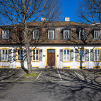 Schloss und Schlossgarten Schwetzingen - Sonstige Bauten - Palais Ysenburg (Forsthausstraße 7 und 9) - Von Nordwest - Blick von der Mauer zum Betriebshof in der Forsthausstraße nach Osten auf die Westseite des Palais Ysenburg; rechts davon (außerhalb des Bildes) befindet sich der Verbindungsbau zum Alten Forstamt (ehemalige Bewohner: Mitglieder des kurfürstlichen Hofstaats, Oberhofgärter Theodor van Wynder († 1777), bis 1778 Oberstjägermeister Graf Friedrich Wilhelm von Ysenburg-Birstein (1730-1804) und Ehefrau Caroline Gräfin von Parckstein 1762-1816), eine uneheliche Tochter von Kurfürst Carl Theodor, Oberstjägermeister Johann Theodor Maria Reichsgraf v. Waldkirch (1720–1802), Oberforstmeister Friedrich Heinrich Georg Freiherr von Drais (1758-1833), ab 1864 der Industrielle Gustav Bassermann und Ehefrau Clementine; nach 1918 Kauf durch Stadt Schwetzingen, seit 1997 in Privatbesitz) (Bau: L-formig; Länge x Breite: Nordflügel ca. 34 x 7 Meter, Westflügel ca. 21 x 13 Meter, Westflügel mit Anbau bis zum Alten Forstamt ca. 48 x 10 Meter; Geschosse: 2 (inkl. Mansardgeschoss); Bauzeiten: 1760, Verbindung zum Alten Forstamt 1775, erweitert Ende des 19. Jh. restauriert 1997; Architekt: wohl Franz Wilhelm Rabaliatti (1714–1782)) (aufgenommen im April 2025, am späten Nachmittag)