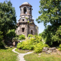 Schloss und Schlossgarten Schwetzingen - Garten - Merkurtempel - Von außen - Von Süden - Blick nach Norden auf den Merkurtempel, als Ruine gebaut; etwas links unterhalb der Bildmitte eine vergitterte Tür, dahinter der Zugang zum Untergeschoss, rechts führt ein Fußweg zum östlichen Eingang (Architekt: Nicolas de Pigage (1723-1796); Bauzeit: 1784-1792, Restaurierung: 2008–2013; Abmessungen: Grundfläche des Sechsecks Länge x Breite ca. 14 x 12 Meter, Länge konkave Portalseiten ca. 10 Meter, Tiefe Kabinettseiten ca. 3,5 Meter, Durchmesser Tambour ca. 6,5 Meter, Höhe ca. 25 Meter, 4 Geschosse) (aufgenommen im Juni 2025, am Nachmittag)