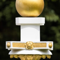 Schloss und Schlossgarten Schwetzingen - Garten - Zwischen Angloisen & Bosketten / Kugelallee - 8 Postamente mit Kugeln - Von Südost - Blick auf Details eines der acht Postamente mit vergoldeten Kugeln; Standort: im Nordwesten des Rasenfeldes; oben eine vergoldete Kugel, darunter eine Platte mit goldenen Rosetten und Kügelchen, darunter ein Kapitell aus Akanthusblättern (Bildhauer: der Werkstatt von Franz Conrad Linck (1730-1793) zugeschrieben; Datierung: um 1770; Material: Sandstein, weiß gefasst; Höhe Gesamt / Sockel: 276 / 33 Zentimeter; Inv.Nr. G 4221-4228; Kopie, Original im Depot) (aufgenommen im Juli 2025, um die Mittagszeit)