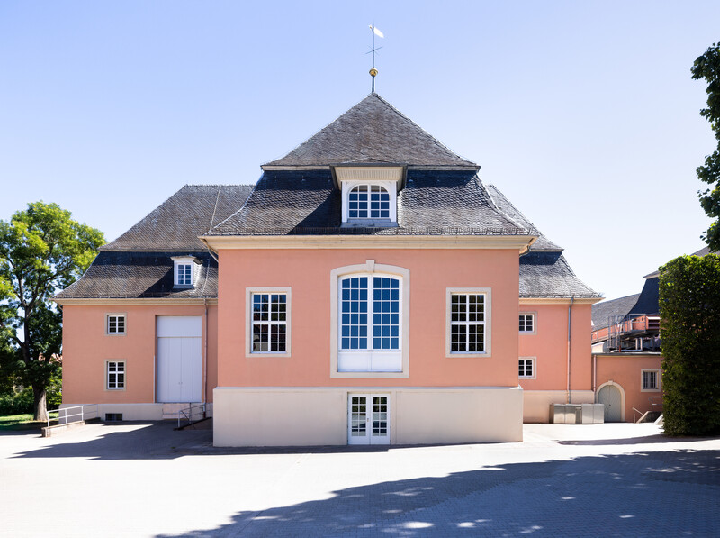 Schloss und Schlossgarten Schwetzingen - Garten - Schlosstheater / Rokokotheater - Von Nordwest - Blick von der Zufahrt zum Theater auf die Westfassade des Theaterbaus; hinter den drei mittleren Fenstern befindet sich die Hinterbühne, hinter dem großen Tor links die Seitenbühne; ganz rechts ein Zwischenbau zwischen dem Theater und dem Nördlichen Zirkelbau; ganz links befindet sich der Gesandtenhausgarten (Gesamter Bau: Länge x Breite: ca. 62 x 35 Meter; Architekt: Nicolas de Pigage (1723-1796); Bauzeit: 1752-1753, Erweiterung 1762, Sanierung: 1937, Renovierung: 1952, Generalsanierung / Umbau 1971-1974, Restaurierung: 1999-2005) (aufgenommen im August 2025, am Nachmittag)
