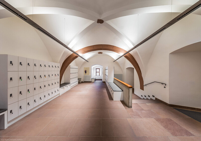 Schloss und Schlossgarten Schwetzingen - Schloss - Mittelbau - Von innen - Erdgeschoss, Nordseite - Besucherzentrum / ehemaliger Hochkeller - Von Westen - Blick von der Mitte des Raums nach Osten in den gewölbten Raum (mit 4 Jochen, 3 Gurtbögen und Kreuzgratgewölben); das östliche Ende des Raums und das kleine Fenster sind Teil des Nordturms; vorne rechts der Durchgang zur Vorhalle des Raums, hinten rechts der Durchgang zum nördlichen Treppenhaus; am Ende des Raums hinter der linken (nördlichen) Wand liegt die Schlosskapelle; im 16. Jahrhundert diente der Raum als Hofstube (eine Art Mensa), später als Hochkeller, ab 2016 als Besucherzentrum; der Boden des Raum lag früher 4 Treppenstufen tiefer, der Raum besaß Zwischenwände, ein Gewölbeschlusstein trägt die Jahreszahl 1521 (Mittelbau: Länge Westseite ca. 45 Meter, Breite Süd-/Nordseite ca. 38 Meter; Wiederaufbau / Erweiterung: 1698-1717; Architekt: Johann Adam Breunig) (aufgenommen im November 2025, am späten Vormittag)