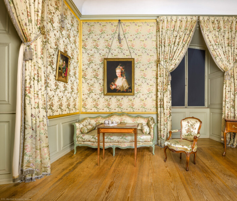 Schloss und Schlossgarten Schwetzingen - Schloss - Mittelbau - Von innen - 1. Obergeschoss - Appartment des Kurfürsten - Kabinett - Von Osten - Blick von der Tür zum Kabinett nach Westen auf eine Sitzgruppe, bestehend aus einem Canapé (Sofa), einem Fauteuil (Polstersessel mit Armlehnen) und einem kleinen Tisch; ganz rechts ein Verwandlungstisch; oberhalb der Bildmitte ein Porträt der Maria Josepha Seyffert (1748-1771, seit 1769 Gräfin von Heydeck), eine Mätresse des Kurfürsten Carl Theodor; links ein Porträt von Kurfürst Carl Theodor (1724-1799, reg. 1742-1799) (aufgenommen im Februar 2026, am späten Vormittag)