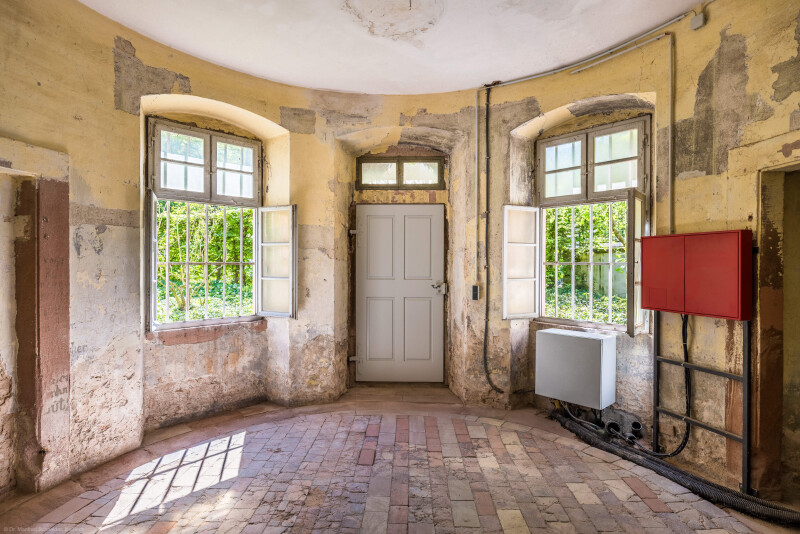 Schloss und Schlossgarten Schwetzingen - Garten - Badhausanlage - Badhausküche - Von innen - Rotunde - Von Nordost - Blick in den runden Eingangsraum, auf die Eingangstür (Mitte) sowie ganz links und ganz rechts auf ehemalige Wandschränke (Gesamter Bau: Länge x Breite (winkelförmig) ca. 13 x 11 Meter, Höhe (über Rotunde) ca. 8 Meter; Raum: Durchmesser ca. 5 Meter, Höhe ca. 3 Meter; Architekt: Nicolas de Pigage (1723-1796); Bauzeit: 1768-1772, Dachinstandsetzung: 1983-1985, Instandsetzung: 2013-2015) (aufgenommen im April 2026, am Nachmittag)