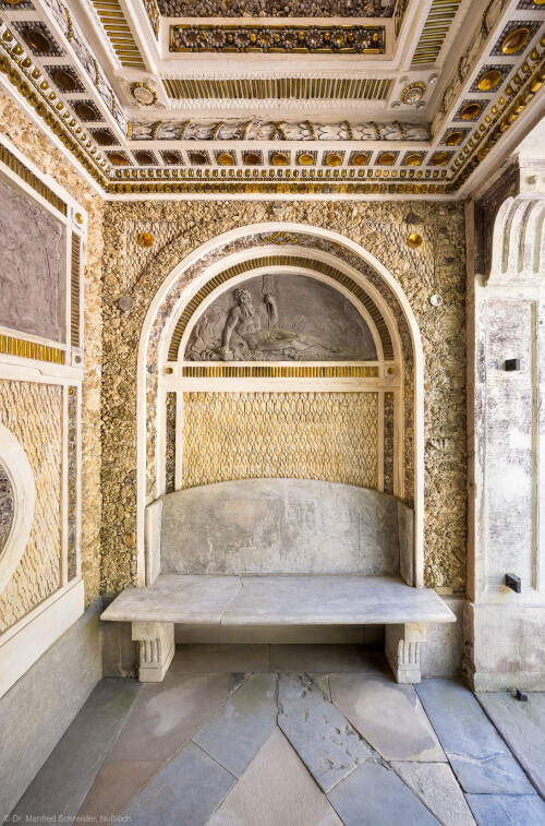 Schloss und Schlossgarten Schwetzingen - Garten - Badhausanlage - Östliches Achathäuschen - Von innen - Südwand - Blick von der nördlichen Ruhebank nach Süden in den Raum, auf die Decke, auf die südliche Wand, auf die Lünette mit einem Bleirelief der Darstellung eines bärtigen Flussgottes sowie auf die südliche Bank (Bildhauer: Franz Conrad Linck (1730-1793), Datierung: um 1770-1775) (Achathäuschen: Abmessungen Breite x Tiefe x Höhe 3,2 x 3,0 x 6,4 Meter, Innenraum Breite x Tiefe ca. 2 x 2 Meter; Architekt: Nicolas de Pigage, Fertigstellung: um 1775, Instandsetzung: 1991 - 1995) (aufgenommen im Mai 2026, am Vormittag)